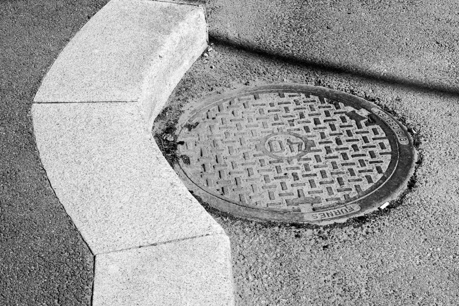 Kum med støpejernslokk i asfalten ved en kantstein